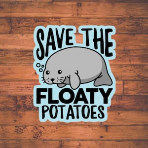 May include: A sticker featuring a cartoon manatee in gray with the text "SAVE THE" above and "FLOATY POTATOES" below, all in black letters on a light blue background. The sticker is set against a brown wood grain background.