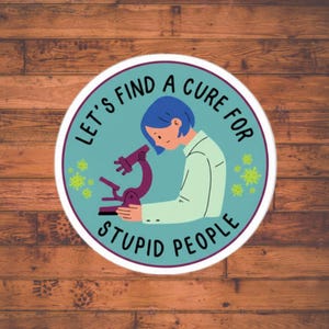 May include: A round sticker with a teal background and the text "LET'S FIND A CURE FOR STUPID PEOPLE" in a circular pattern. The image features a person with blue hair looking into a purple microscope.