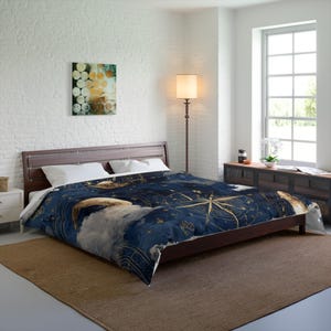 May include: A dark blue comforter with a celestial design featuring gold compasses, stars, and a crescent moon. The bedding is on a wooden bed frame in a well-lit bedroom. A painting hangs on the wall.
