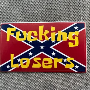 May include: Rectangular sticker with a red background and a blue and white cross design. The sticker has yellow text that reads "Fucking Losers". The design includes white stars.