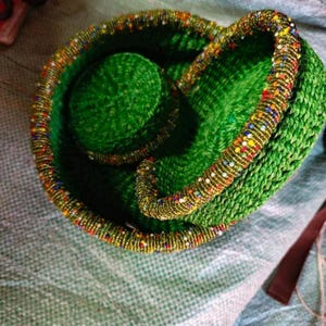May include: A green woven basket with a beaded edge. The basket features a circular design with a central, raised circle. The rim is decorated with colourful beads, enhancing the basket's overall aesthetic appeal.