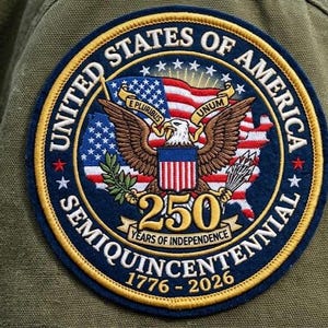 May include: A circular patch with a blue border and gold lettering, commemorating the 250th anniversary of the United States of America's independence. The patch features a bald eagle, the American flag, and the years 1776-2026.
