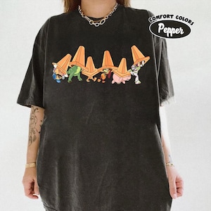 May include: Dark gray Comfort Colors t-shirt featuring a cartoon graphic of characters from a popular animated film. The characters are shown carrying orange traffic cones. The text "Comfort Colors Pepper" is printed on the upper right.