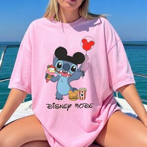 Peut inclure: T-shirt rose clair avec un personnage de dessin anim&eacute; tenant une glace, un ballon et des aliments. Le personnage est bleu avec de grandes oreilles et un chapeau noir. Les mots "Disney Mode" sont imprim&eacute;s en dessous.