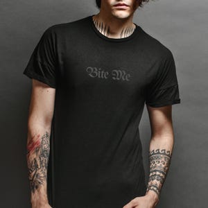 Black unisex gothic shirt with subtle “Bite Me” text design worn by model, minimalist dark humor graphic tee