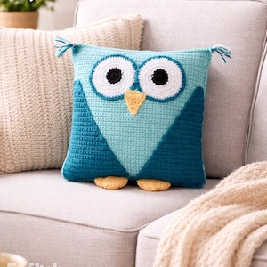 Könnte beinhalten: Gehäkeltes Eulen-Kissen in Türkis und Blau mit großen weißen und schwarzen Augen und einem gelben Schnabel. Das Kissen hat kleine, getuftete Ohren und Füße. Der Text "PDF PATTERN" ist sichtbar.