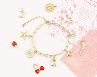 May include: A gold charm bracelet featuring a variety of pendants, such as a starfish, moon, cherry, and turtle. Other charms include a paw print, a coin with an eye, a star, a horn, and a rectangular charm. The bracelet is set against a pink floral backdrop.