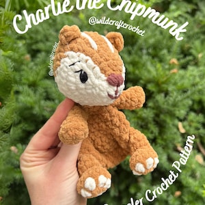 Può includere: Un giocattolo di scoiattolo a strisce all'uncinetto, marrone e bianco, con il testo "Charlie the Chipmunk" e "Snuggler Crochet Pattern". Lo scoiattolo ha una pancia bianca, un naso marrone e occhi neri. Lo sfondo è un fogliame verde.