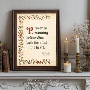 Könnte beinhalten: Gerahmter Druck mit dem Zitat „Gebet ist, vor Gott zu stehen mit dem Geist im Herzen“. Der Druck hat einen braunen Rahmen und ist mit floralen Akzenten verziert. Die Szene umfasst brennende Kerzen und einen dekorativen Kaminsims.