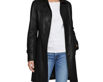 May include: A black leather trench coat with a button-up front, lapel collar, and long sleeves. The coat is worn over a white top and blue jeans. The coat has a classic, tailored design.