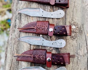 May include: Three metal knife blades with copper-colored wavy lines and three matching dark brown leather sheaths featuring embossed patterns, leather lacing, and silver-toned metal snap closures, arranged in an alternating vertical row.