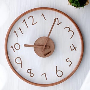 May include: A circular wooden wall clock with a transparent face. The clock features brown numerals and hands, and a brown wooden frame. The clock face has the word "Banana" printed on it.