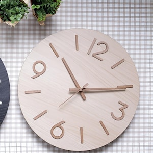 May include: A light wood-effect wall clock with a minimalist design. The clock has raised, light brown numerals and hands. The clock's face is a light wood grain, and the hands show the time. The clock is round.