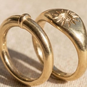 Könnte beinhalten: Eine weiße Keramik-Tasse mit schwarzem Henkel und dem Text "But First, Coffee" in schwarzer, handschriftlicher Schrift. Die Tasse steht auf einer weißen Oberfläche.