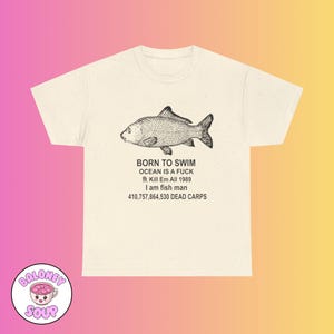 May include: Cream-colored t-shirt featuring a detailed black illustration of a fish. Below the fish, the text reads "BORN TO SWIM OCEAN IS A FUCK 魚 Kill Em All 1989 I am fish man 410,757,864,530 DEAD CARPS".