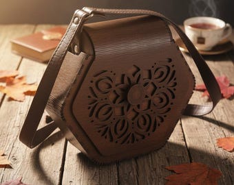 May include: A brown wooden handbag with a laser-cut floral design on the front. The bag has a shoulder strap and a clasp closure. The bag is sitting on a wooden surface with autumn leaves.