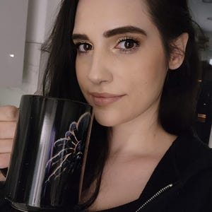 Peut inclure: Une tasse en céramique noire ornée d'un motif détaillé représentant une mygale aux pattes poilues avec des reflets bleu foncé et violets. La tasse présente une finition brillante et une forme cylindrique, avec une anse latérale bien visible.