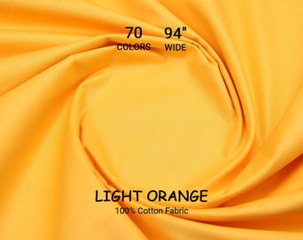 Op de afbeelding: Lichtoranje 100% katoenen stof, 239 cm breed. De afbeelding toont een close-up van de stof met de tekst "70 KLEUREN" en "LICHT ORANJE". De stof is effen van kleur.