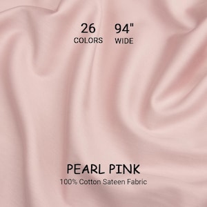 Könnte beinhalten: Perlrosa 100% Baumwoll-Satin-Stoff, 239 cm breit. Das Bild zeigt eine Nahaufnahme des Stoffes mit weichen Falten. Der Text weist auf 26 Farben hin. Der Stoff ist ein helles, pastellrosa.
