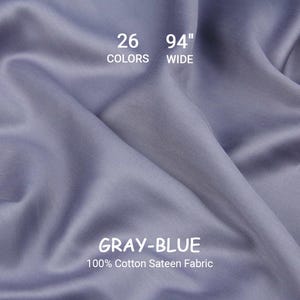 以下が含まれることがあります： グレーブルーの綿100％サテン生地、幅239cm。生地は柔らかく、流れるような素材で、折り目やハイライトが見えます。画像には「26色」という文字も含まれています。