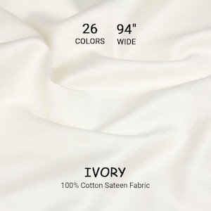 May include: Ivory-coloured 100% cotton sateen fabric. The fabric is 239 cm wide and available in 26 colours. The fabric is draped, showing soft folds and texture. The text "IVORY" and "100% Cotton Sateen Fabric" are displayed.