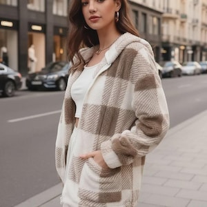 May include: A brown and white plaid hooded jacket with a zipper closure. The jacket has a soft, fuzzy texture and two front pockets. The person is wearing a white top and skirt. The background shows a city street with cars and buildings.