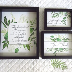 May include: Three framed wall art prints with a green leafy design and inspirational quotes. The first print says "They broke bread in their homes and ate together with glad and sincere hearts Acts 2:46". The second print says "Taste and see that the Lord is good Psalm 34:8". The third print says "In everything give thanks 1 Thessalonians 5:18".