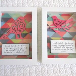 May include: Two framed wall art pieces featuring a pink bird cutout against a geometric patterned background. The text in the frames reads "Consider the birds... they do not sow or reap or store away in barns, and yet your heavenly Father feeds them. Are you not of more value than they?" Matthew 6:26