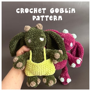 May include: Two plush goblin dolls made of textured yarn. The front doll is dark green with a lime yellow top, while the back doll is magenta. Both have large ears, small horns, and light-colored accents. Text reads: CROCHET GOBLIN PATTERN.