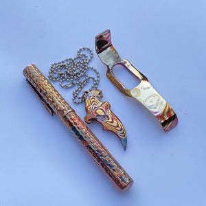 May include: A collection of metal accessories with a colorful, iridescent finish. Includes a pen, a bottle opener, and a pendant with a chain. The pen and bottle opener have a textured surface.