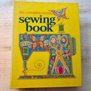 May include: A vintage sewing book with a bright yellow cover. The title "the complete family sewing book" is in blue and the cover features a colorful illustration of a sewing machine, scissors, and a butterfly.