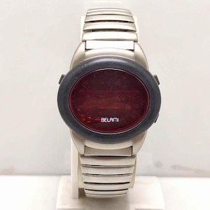 Puede incluir: Reloj digital Belami vintage con una correa de metal plateado y un bisel negro. La esfera del reloj es de color rojo intenso y se ve el nombre de la marca "BELAMI". El reloj tiene un dise&ntilde;o retro y futurista.