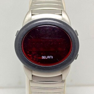 Puede incluir: Un reloj digital Belami vintage con una correa de metal plateado. La esfera del reloj es de forma ovalada roja oscura, rodeada por un bisel negro. La palabra "BELAMI" est&aacute; impresa en blanco en la esfera.