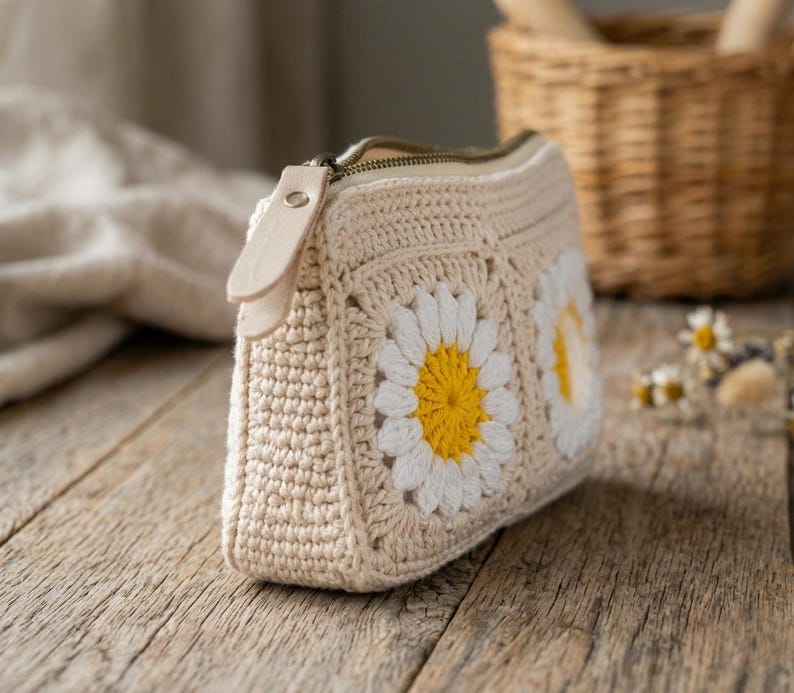 Crochet cosmetic pouch featuring daisy granny squares, textured cotton stitches, and zippered top, perfect for makeup storage and travel accessories.