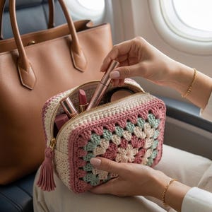 Może przedstawiać: Ręcznie robiona kosmetyczka z szydełka w wzór granny square, w odcieniach różu, kremu i miętowej zieleni. Posiada złoty zamek błyskawiczny i pasujący chwost. Wewnątrz znajdują się szminki, puder i tusz do rzęs. W tle brązowa skórzana torba.