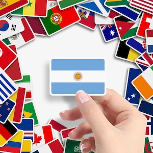 May include: A sticker of the Argentinian flag, light blue and white with a sun emblem, is held by a hand. Various national flags surround the sticker, including flags from different countries.