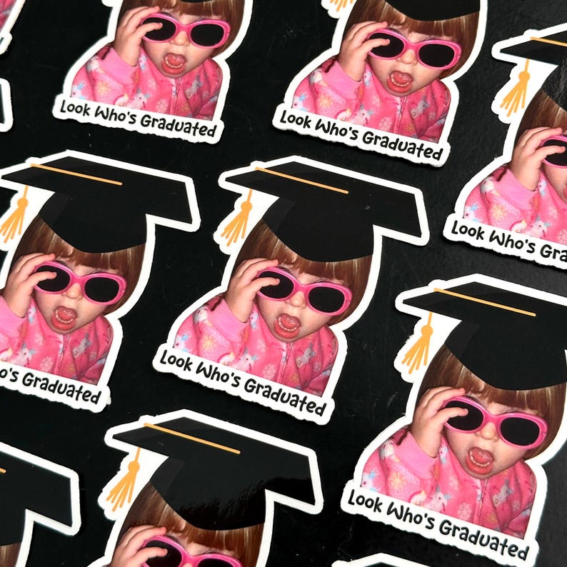 May include: Sticker sheet featuring multiple stickers of a child wearing pink sunglasses and a graduation cap. The stickers have the text "Look Who's Graduated" in white.