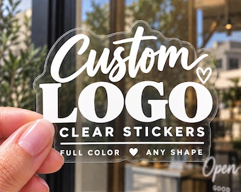 May include: A clear adhesive sticker featuring white text that reads Custom LOGO CLEAR STICKERS, with the additional text FULL COLOR, a heart icon, and ANY SHAPE. The sticker has a die-cut edge that follows the contour of the lettering and design.