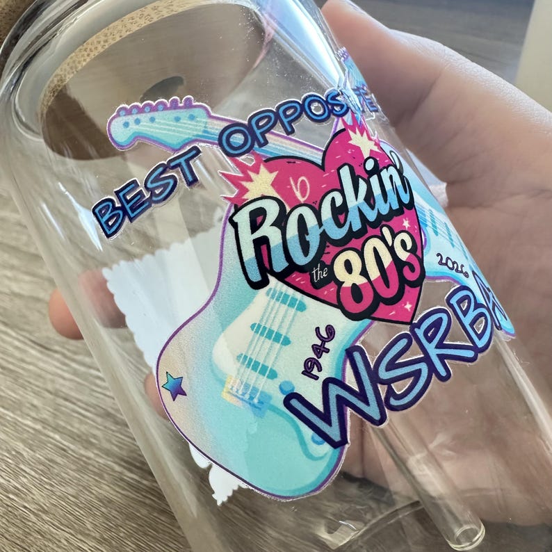 May include: A clear glass tumbler with a bamboo lid and a glass straw, featuring a colorful decal of a light blue electric guitar, a pink heart, and the text "BEST OPPOSITE", "Rockin the 80's", "1946", "2026", and "WSRBA".