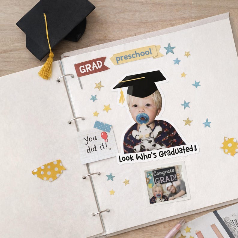 May include: A scrapbook page with graduation-themed decorations. Includes a photo of a baby wearing a graduation cap and holding a stuffed animal, with the text "Look Who's Graduated!" and "Congrats Grad!" Also features star stickers and a miniature graduation cap.