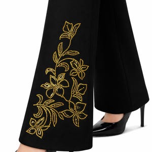 May include: Black flared pants with a gold floral design on the side. The floral pattern is made of small, gold-colored embellishments. The pants are paired with black high-heeled shoes.