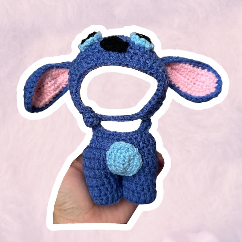 K&ouml;nnte beinhalten: Blaues H&auml;kelm&uuml;tzen- und Shorts-Set, das die Figur Stitch darstellt. Die M&uuml;tze hat gro&szlig;e Ohren mit rosa Innenfutter, schwarze und blaue Augen und eine schwarze Nase. Die Shorts haben einen hellblauen Pompon auf der R&uuml;ckseite. Handgefertigt.
