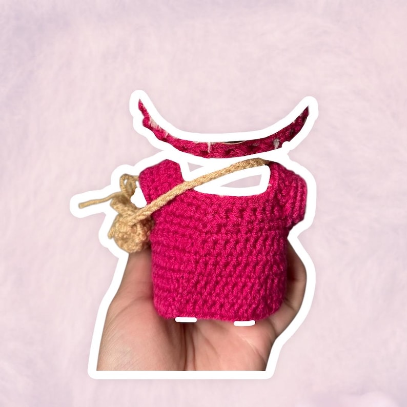 Puede incluir: Un top de ganchillo rosa intenso hecho a mano con una peque&ntilde;a bolsa de ganchillo beige sujeta con una correa beige. Una forma de media luna rosa intenso a juego est&aacute; encima del top. El trabajo de ganchillo es visible y detallado.
