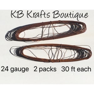 May include: Two spools of 24 gauge copper wire, each spool containing 30 feet of wire. The wire is brown in color and is coiled in a circular shape. The text "KB Krafts Boutique" is printed at the top of the image and the text "24 gauge 2 packs 30 ft each" is printed at the bottom of the image.