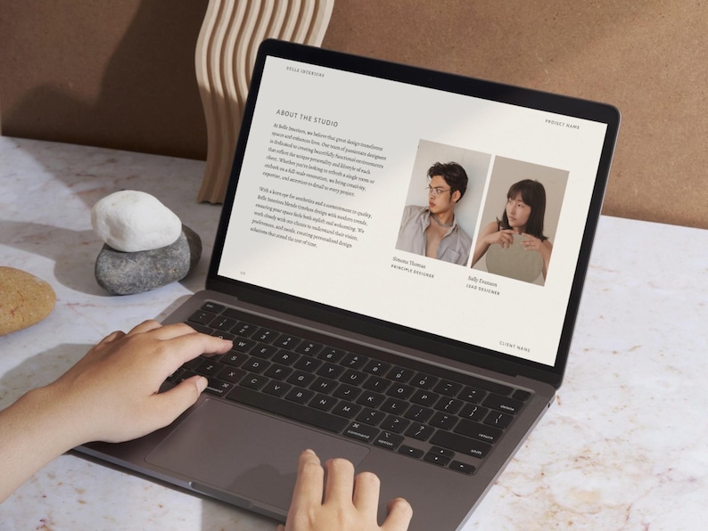 Puede incluir: Un ordenador port&aacute;til muestra un sitio web con texto y dos fotos de perfil. La pantalla muestra las palabras "About The Studio" y los nombres de dos personas. Se ven manos tecleando en el teclado. Piedras decorativas y una escultura de madera en el fondo.
