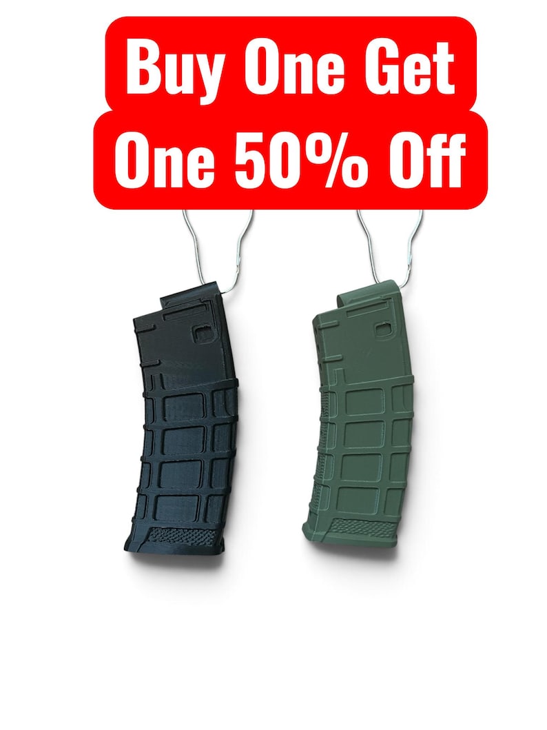 May include: Two polymer firearm magazines, one black and one olive green, each featuring a textured grid pattern and a metal wire hanger. Above the magazines is a red rectangular sign with white text that reads Buy One Get One 50% Off.