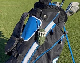 May include: A black and blue golf bag with a stand, featuring a green grenade-shaped golf tee holder attached to the side. The bag contains several golf clubs with metal heads and black grips, and the exterior has white trim and blue accents.