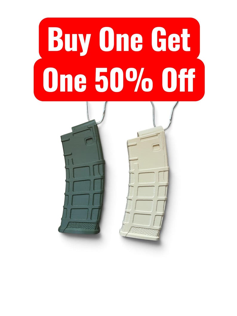 May include: Two rifle magazines, one olive green and one tan, hang from metal hooks. Above them, a red rectangular sign with rounded corners displays the white text: Buy One Get One 50% Off. The magazines feature a grid-like textured surface.