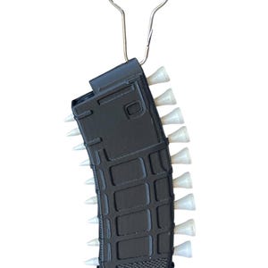 May include: A black, rectangular, textured magazine-shaped keyring featuring a series of small, white, cone-shaped golf tees inserted along both sides. The object is attached to a silver-coloured metal keyring loop at the top.