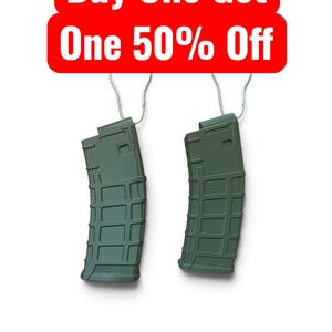 May include: Two olive green polymer rifle magazines with a textured grid pattern on the exterior, each suspended by a silver metal hook. Above the magazines, a red rectangular sign displays the white text Buy One Get One 50% Off.